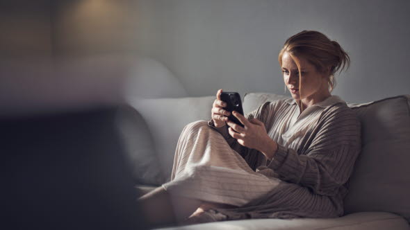 Kvinna som sitter i en soffa och läser på om fonder i sin mobiltelefon.