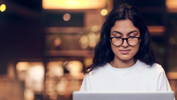 Ung kvinna som sitter och tittar ner i sin laptop